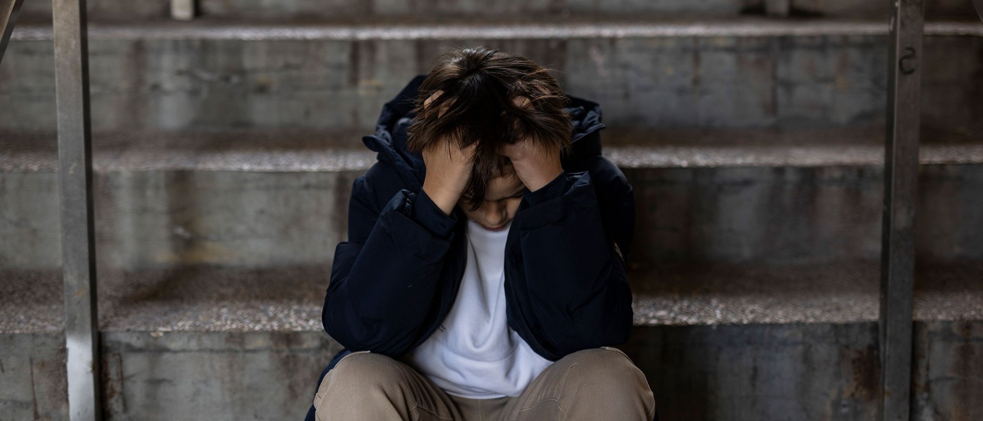 Un niño sentado en una escalera con las manos en la cabeza y con sensación de estar agobiado por algo.