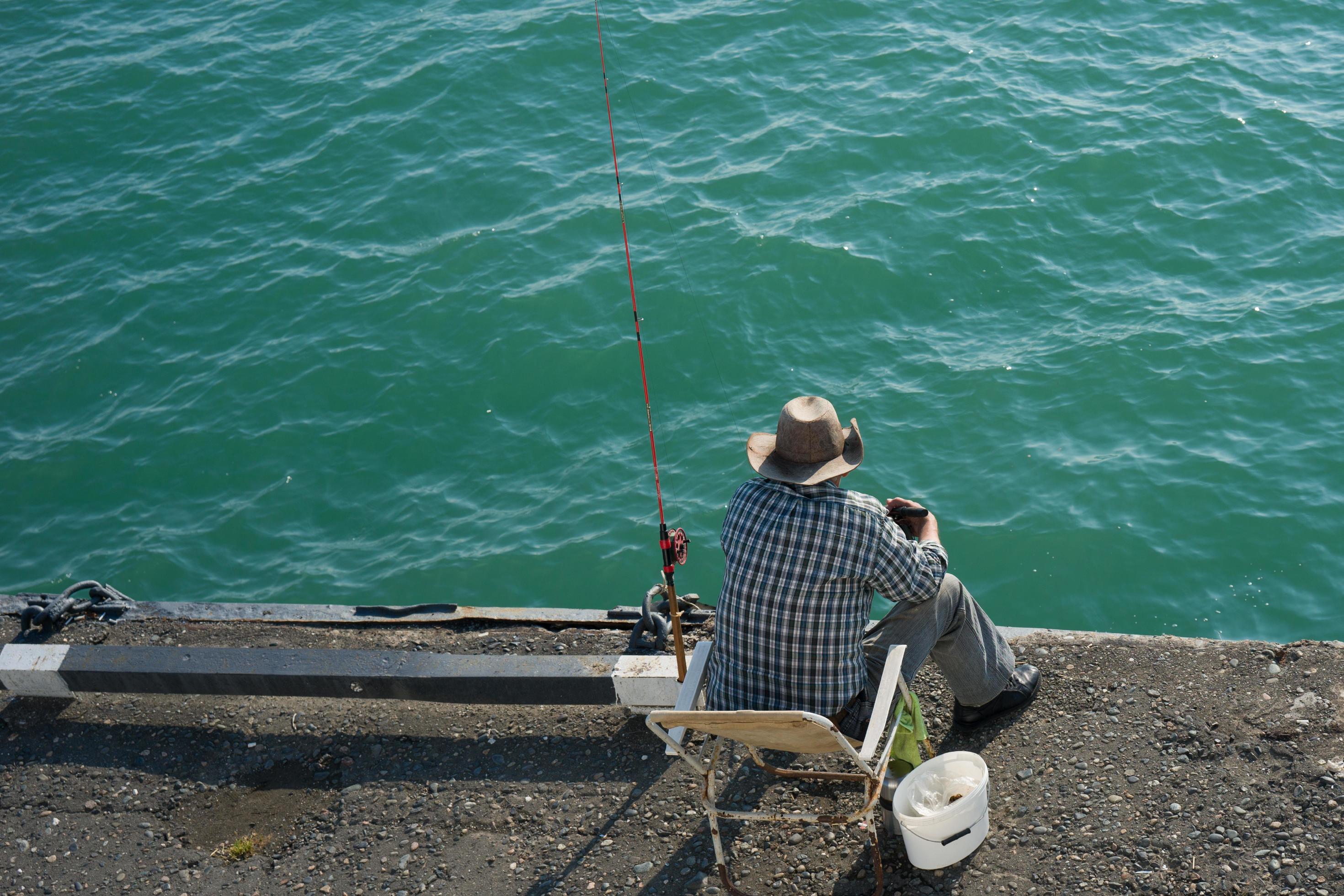 Hombre sentado en una silla de camping mientras pesca junto al mar
