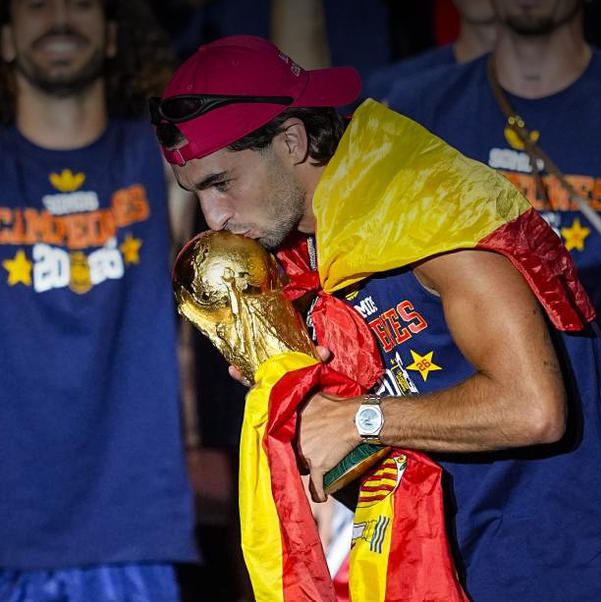 Ferran Torres besando la copa del Mundial con la bandera de España como capa y la famosa gorra trumpista.