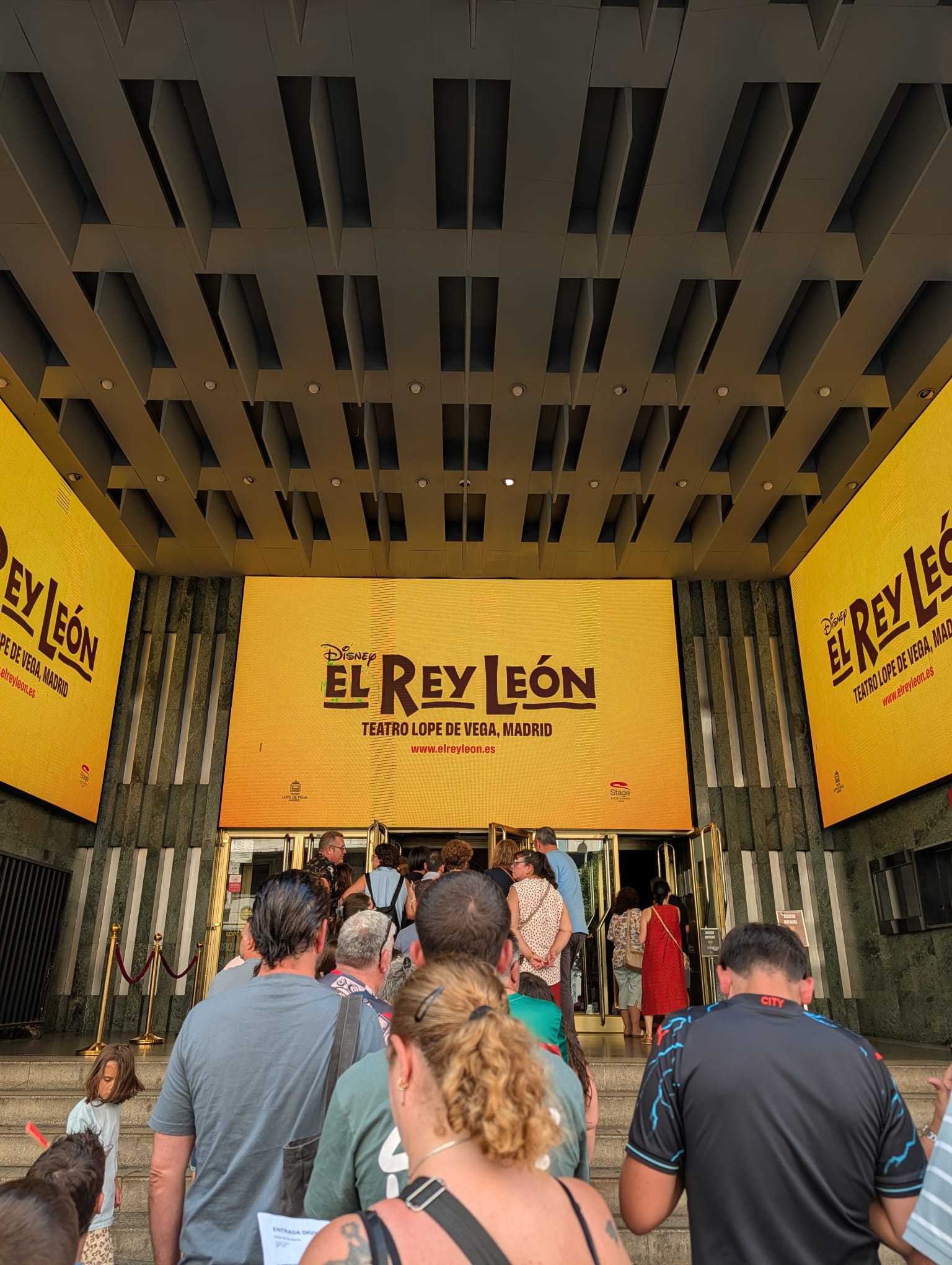Entrada al teatro para ver El Rey León. Se puede ver la cola de gente y un cartel en el fondo con la obra.